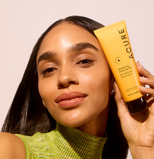 Woman holding a tube of Acure skincare product against a plain background