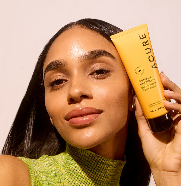 Woman holding a tube of Acure skincare product against a plain background