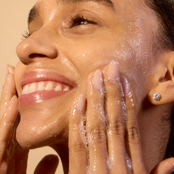 Woman washing her face with a beige background