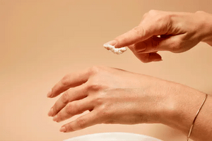 Person applying cream to their hand against a beige background